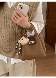 Detail of dark brown pebble leather bucket bag with metal lock and cute bear charm