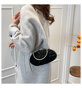 Detail of black oval clutch with pleated texture, gold handle and chain on a grey coat