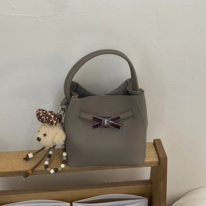 Detailed close-up of taupe bucket bag featuring metal bow clasp and teddy bear charm