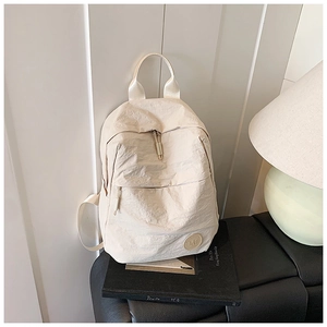 Gros plan du sac à dos beige en tissu texturé avec poche zippée et logo M rond