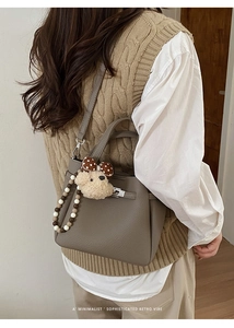 Detail of grey leather bucket bag with silver metal clasp and plush bear charm pendant