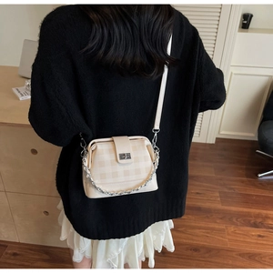 Detail of cream crossbody bag with checkered texture and silver chain strap
