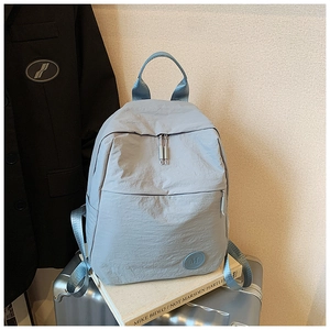 Détail du sac à dos en nylon bleu-gris montrant le patch logo M et la fermeture éclair