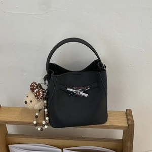 Detail of black lychee grain leather bucket bag with silver bow clasp and bear charm