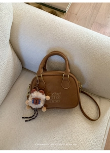 Detailed close-up of brown vintage bowling bag featuring an alpaca charm on a plush sofa