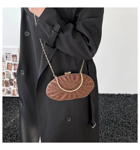 Detail of a brown oval evening bag with rippled texture and golden chain on a model