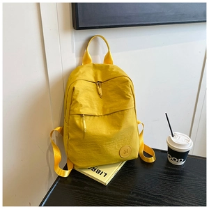 Détail d'un sac à dos en nylon jaune avec logo M, fermeture zippée et bretelles réglables