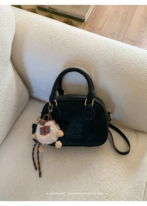 Detail of black suede bowling bag with gold hardware and brown plush animal keychain