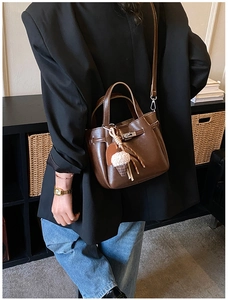 Detail of a brown leather bucket bag featuring a classic lock and ice cream charm