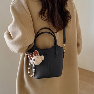 Detail der schwarzen Beuteltasche mit Bärenanhänger an Modell im beigefarbenen Mantel