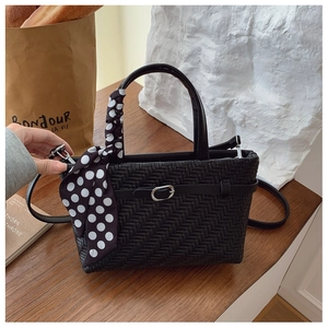 Close-up of black woven leather handbag featuring a polka dot scarf and metal buckle detail