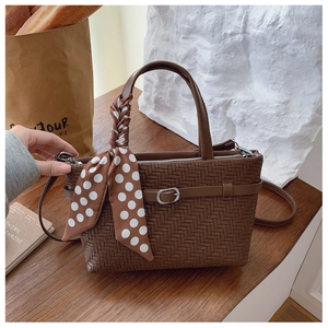 Detailed view of dark brown woven texture handbag with polka dot scarf on a wooden table