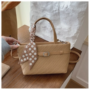 Detail of woven texture handbag with polka dot scarf handle on a wooden cafe table