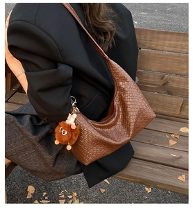 Detail of a brown woven leather hobo bag with a plush monster charm on a wooden bench