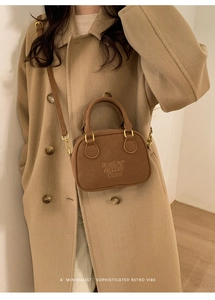 Brown vintage bowling bag with matte leather and adjustable strap on a wool coat