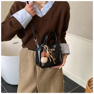 Detail of black leather bucket bag with silver twist lock and heart pompom charm
