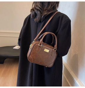 Close-up of a brown vintage leather handbag with gold metal plaque and shoulder strap
