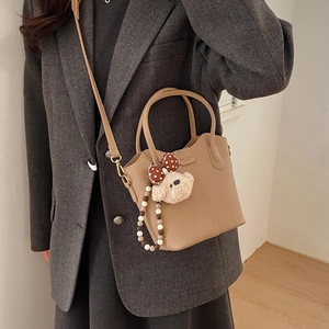 Details der großen khakifarbenen Beuteltasche mit Litschi-Textur und süßem Bärenanhänger