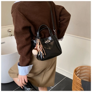 Detail of black bucket bag featuring silver turn-lock clasp and plush ice cream charm