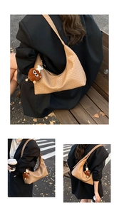 Close-up of brown woven hobo bag with plush doll charm against autumn leaves