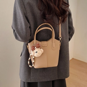 Detail der hellbraunen Eimer-Tasche mit Lederkörnung und einem niedlichen Plüschbär-Anhänger