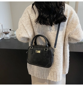 Classic black vintage small square bag worn over the shoulder by a model in a cafe