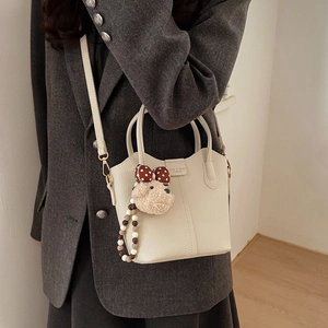 Detail der cremeweißen Beuteltasche mit süßem Bärenanhänger und Perlenkette für Damen