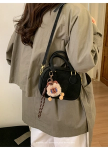 Close-up of retro black crossbody bag with double handles and a cute plush charm