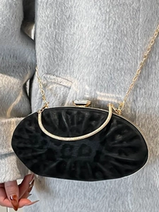 Elegant black shell evening bag with gold chain and pleated texture on grey coat