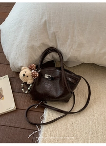 Detail of dark brown leather bucket bag with silver metal lock and cute bear charm