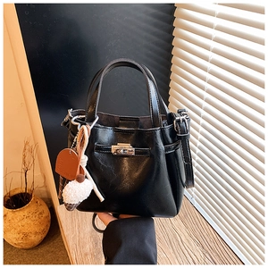 Detail of black bucket bag with silver twist lock and fluffy decorative pendant charm