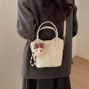 Detailansicht der beigen Leder-Beuteltasche mit Plüschbär-Anhänger und Perlenkette