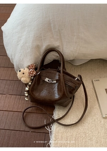 Detail of retro dark brown leather handbag featuring a metal lock and teddy bear charm