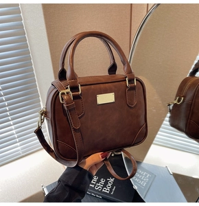 Detail of vintage brown leather handbag with gold metal plaque and round handles
