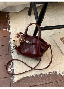 Close-up of retro wine red polished leather handbag with bear charm on soft white rug
