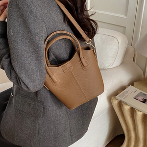 Detailansicht der braunen Leder-Eimertasche mit Textur, getragen von einem Model zu Hause
