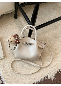 Detail of off-white textured leather bucket bag with silver twist lock and bear charm