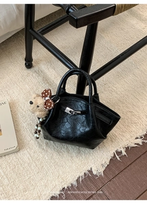 Close-up of black leather bucket bag with silver buckle and plush bear charm on a rug