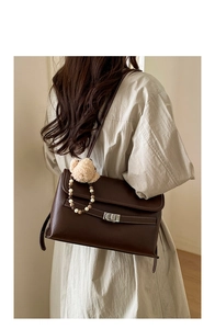 Detail of a dark brown matte leather shoulder bag with silver clasp and plush bear charm