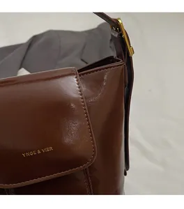 Close-up of brown glossy leather shoulder bag with golden buckle and fine texture detail