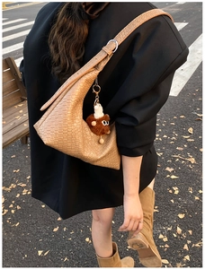 Close-up of light brown woven half-moon tote bag with cute plush monster charm