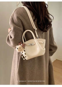 Detail view of beige mini crossbody bucket bag with bear pendant and silver lock