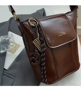 Detail of dark brown glossy bucket bag with golden abacus charm and brand logo