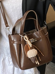 Minimalist dark brown bucket bag with plush charm and crossbody strap for winter 2025