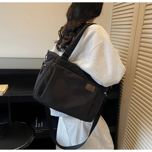 Détail d'un sac cabas en nylon noir avec écusson logo en cuir marron porté à l'épaule