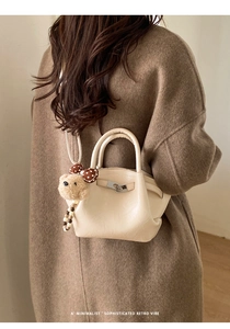 Detail of minimalist beige bucket bag featuring silver buckle and cute teddy bear charm
