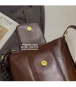 Detail of magnetic buckle closure on a retro dark brown leather bucket bag with stitching