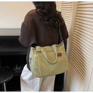 Détail d'un sac cabas vert clair montrant la texture lisse et l'écusson du logo