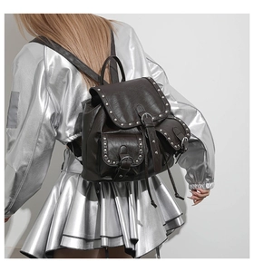 Détail d'un sac à dos punk marron avec clous argentés porté par un mannequin en veste argent