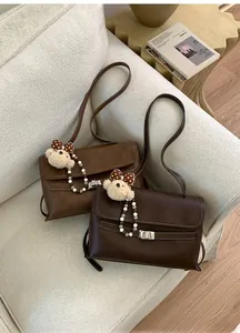Detailed close-up of brown crossbody bags with white stitching and plush bear charms